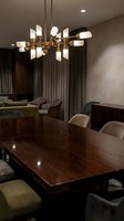 Modern brass chandelier with frosted glass shades illuminates contemporary dining room with dark wood table, neutral upholstered chairs, and floor-to-ceiling curtains for interior design projects.