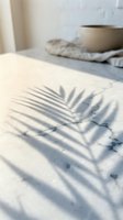 Minimalist interior scene with palm leaf shadow cast on white surface, ceramic bowl on neutral textile, natural sunlight creating geometric patterns for home decor and design projects.