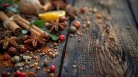 Aromatic spices scattered on rustic wooden table - star anise, cinnamon sticks, nutmeg and pink peppercorns with fresh citrus leaves create cozy holiday mood.