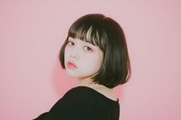 Young Asian woman with short black bob haircut and bangs looking over shoulder against pink background, wearing black top. Natural makeup and soft lighting create gentle mood.