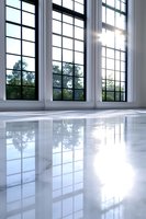 Sunlight streams through tall windows reflecting on glossy marble floor in empty modern interior space, creating dramatic shadows and light patterns.