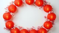 Red paper lanterns arranged in circular wreath with pink cherry blossom branches on white background for Chinese New Year celebration and Asian festival decor.