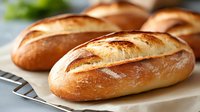 Fresh baked crusty French bread loaves with golden brown crust on cooling rack, close up view of artisanal bakery products against light background.