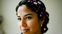 Young woman with dark hair adorned with colorful flowers and pearls, smiling at camera. Suitable for beauty, wellness, and lifestyle marketing materials.
