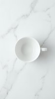 Empty white ceramic cup on marble surface, overhead view for beverage, coffee, tea, and kitchen design projects.