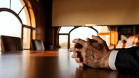 Senior businessman hands clasped on wooden conference table in modern boardroom with warm lighting for corporate meetings and business negotiations.