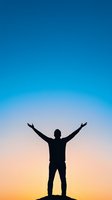 Silhouette of man with raised arms against vibrant blue and orange sunset sky, standing on hill expressing freedom, achievement and life success.