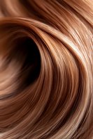 Smooth wavy brown hair strands in close-up macro shot showing glossy texture and natural highlights. For beauty, fashion and hairstyling promotional materials.
