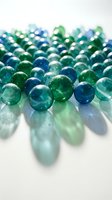 Colorful glass marbles in shades of blue, teal, and green scattered on a white surface, casting soft shadows with light reflections.