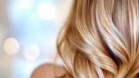 Luxurious blonde wavy hair closeup with soft bokeh background showing professional salon styling and healthy shine. Natural highlights and balayage technique.