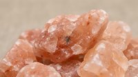 Rough pink salt crystals clustered together on neutral surface, suitable for wellness, spa, mineral, and natural product photography.