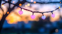 String of glowing pink heart-shaped lights against blurred sunset sky with bokeh effect creates romantic mood for Valentine's Day, wedding or celebration design.