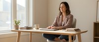 Professional businesswoman working at modern wooden desk in bright office space with natural lighting and minimalist decor for corporate lifestyle content.