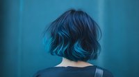 Young Asian woman with vibrant blue dyed hair in bob cut style shown from behind against turquoise background, expressing individuality and modern beauty trends.