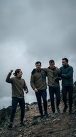 Group of four men jogging together on rocky terrain under overcast sky. Caucasian males wearing athletic fleece jackets and running gear during outdoor fitness training session.