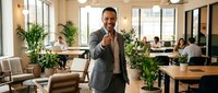 Confident African American businessman giving thumbs up in modern office workspace with colleagues working in background.