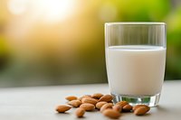 Fresh almond milk in glass with raw almonds scattered on light surface against blurred natural background, healthy dairy alternative beverage.