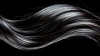 Flowing dark hair strands with silver highlights creating elegant waves against black background for beauty and haircare concepts.