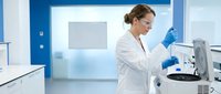 Female scientist in white lab coat conducting research with laboratory equipment in modern blue medical facility for pharmaceutical development.