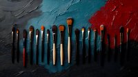 Professional makeup brushes arranged in row against dramatic textured background combining deep turquoise and red tones, creating artistic cosmetic still life.