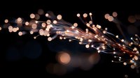 Glowing fiber optic strands with warm bokeh lights creating magical atmosphere against dark background, modern technology and communication concept.
