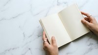 Open blank notebook with hands on marble surface, ideal for journaling, planning, writing, and creative projects.