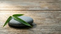 Zen spa stones with fresh green bamboo leaves on rustic wooden background for wellness meditation and natural therapy treatments.