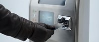 Young adult male wearing black leather gloves inserting credit card into ATM machine for cash withdrawal or banking transaction.