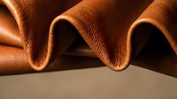 Luxurious brown leather material with elegant curved folds showcasing rich texture and craftsmanship for premium fashion and interior design projects.