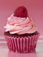 Chocolate cupcake with pink frosting and fresh raspberry on top in paper liner against pink background for bakery and dessert marketing.