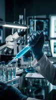 Scientist in protective gloves holding blue liquid test tube in modern laboratory with equipment and glassware for research and analysis experiments.