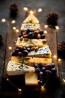 Festive cheese board arranged in Christmas tree shape with grapes, nuts and warm lights on rustic wooden background for holiday entertaining.