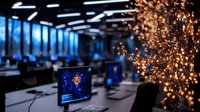 Modern office workspace with glowing fairy lights creating cozy atmosphere, computer monitors on desks, blue evening light through windows, contemporary interior design.