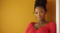 Young African American woman in red dress smiling confidently against yellow wall background, natural curly hair styled up, professional portrait with warm lighting and soft focus.