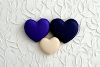Three decorative hearts in navy blue and cream colors arranged on textured white background with floral pattern relief, romantic minimal composition for wedding design.