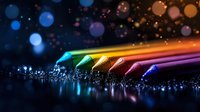 Vibrant rainbow colored pencils arranged in line with water droplets and bokeh light effects creating magical artistic atmosphere on dark background.