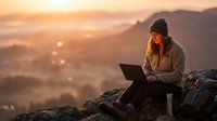 Woman working on laptop at sunrise on mountain peak overlooking misty valley landscape, remote work and digital nomad lifestyle concept for business and technology projects.