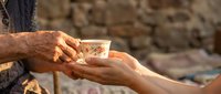 Elderly hands passing traditional coffee cup to younger person in warm sunlight, representing generational connection and hospitality in rustic setting.
