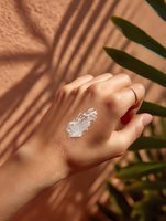 White moisturizing cream sample on female hand with palm leaves shadow on beige background. Natural skincare and organic cosmetics concept.