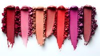 Crushed makeup powder swatches in vibrant red and pink tones arranged in parallel stripes with scattered powder texture showing cosmetic pigment intensity.