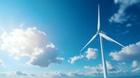 Modern wind turbine against bright blue sky with white fluffy clouds and sunlight. Clean renewable energy generation and sustainable power technology concept.