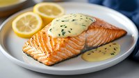 Grilled salmon fillet with creamy hollandaise sauce and fresh herbs, served on white plate with lemon slices, close up view of gourmet seafood dish.