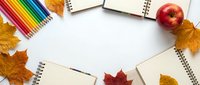 Autumn school supplies with colorful pencils, notebooks and fall leaves arranged on white background for back to school season and educational projects.