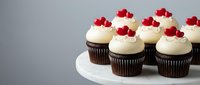 Chocolate cupcakes with white frosting and red heart decorations on white cake stand against gray background for romantic celebrations.