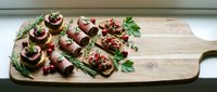 Gourmet appetizer platter with stuffed mushrooms, bacon-wrapped bites and herb-crusted canapes on wooden cutting board for entertaining and party catering.