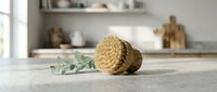 Natural sisal body brush with eucalyptus branch on marble counter in modern kitchen interior for spa wellness and eco-friendly skincare routine.
