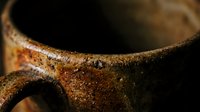 Rustic ceramic coffee mug with weathered brown glaze showing natural wear and texture against dark background for cozy morning beverage concepts.