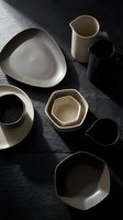 Modern ceramic tableware collection in neutral tones on dark slate surface. Minimalist dinnerware set with organic shapes for contemporary dining and kitchen styling.