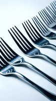 Row of shiny metallic forks with black tines arranged diagonally on white background, suitable for dining, kitchenware, and tableware design projects.