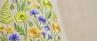 Delicate wildflower embroidery with yellow buttercups, purple cornflowers and green ferns on cream fabric. Botanical needlework design for crafting projects.